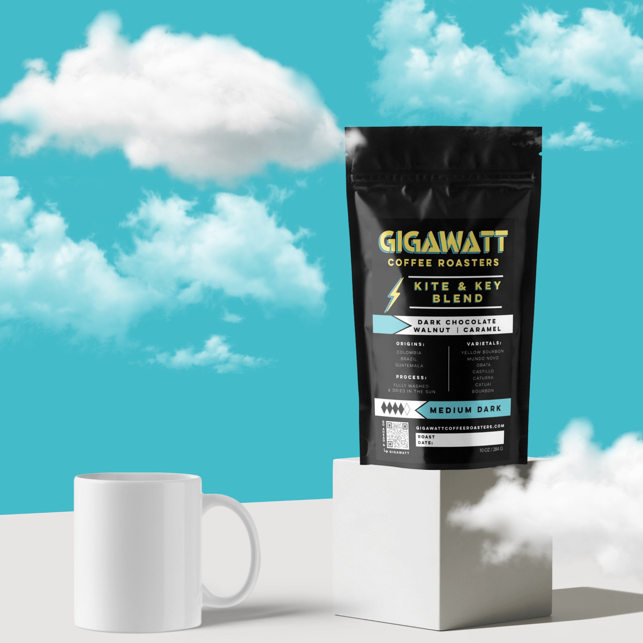 Gigawatt Coffee Roasters Kite & Key Blend featuring notes of dark chocolate, walnut, and caramel, displayed on a pedestal with a white mug and a bright blue sky background with clouds.